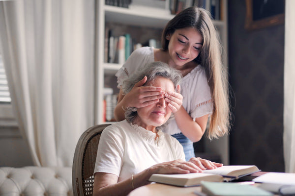 A lady reading a book with her grand daughter stood behind her covering her eye