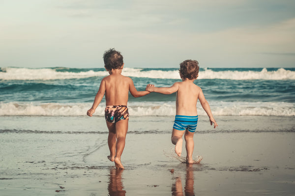 two young boys holding hands whilst running into the sea