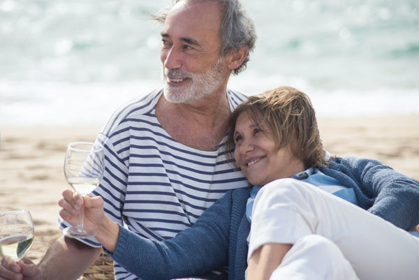 A retired couple sat on the beach with a glass of wine